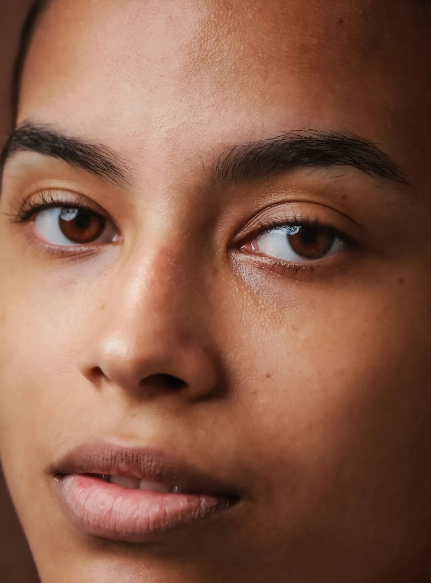 Nahaufnahme eines jungen Gesichts mit ebenmäßiger, natürlicher Haut und dunklen Augen, Modellaufnahme zum Lipofilling mit Eigenfett in Düsseldorf