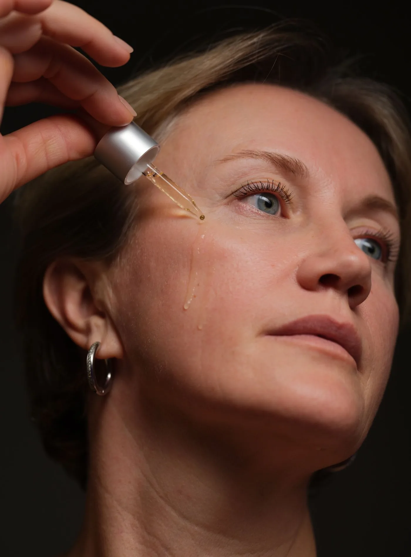 Reife Frau trägt mit einer Pipette Serum auf die Wange auf, Hautpflege, Modellaufnahme zur PRP Therapie in Düsseldorf