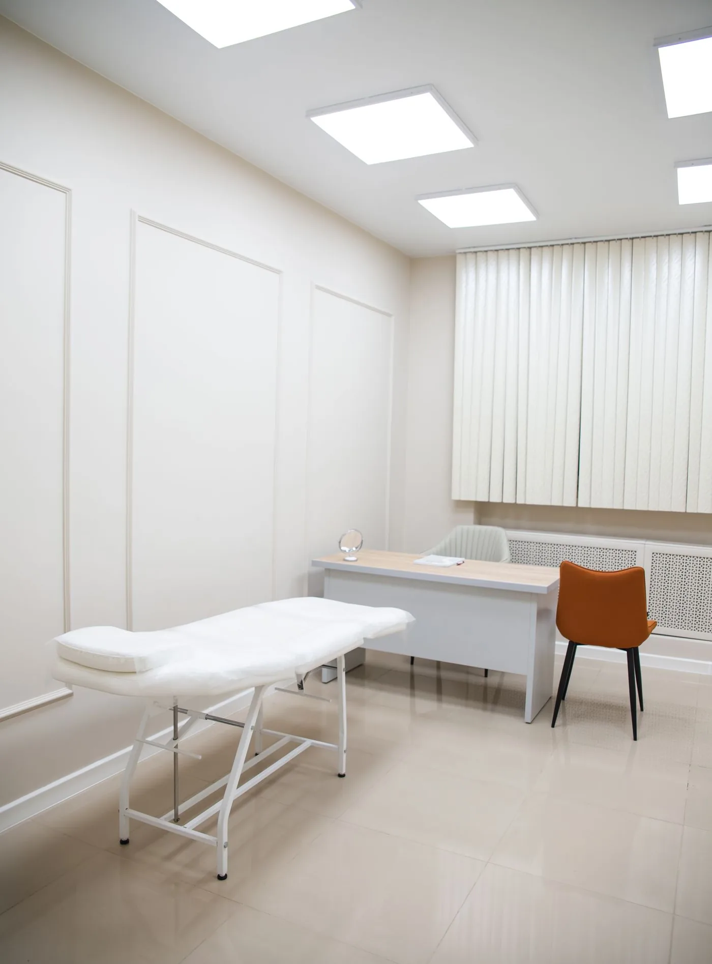 Heller Behandlungsraum mit Liege, Schreibtisch und Stuhl, Symbolbild zum Ratgeber Ästhetische Chirurgie in Düsseldorf