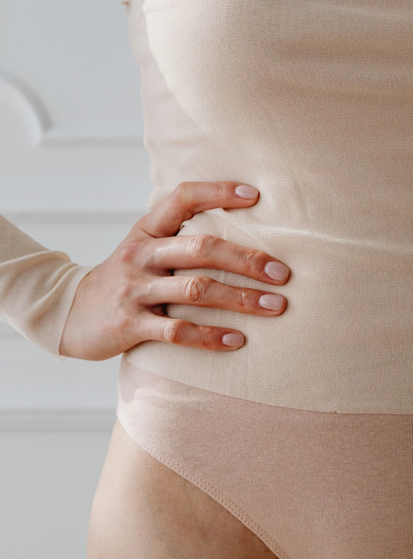 Hand an der Taille einer Frau im beigen Body, Symbolbild für die Körperkontur, Modellaufnahme zur Hip Dips Korrektur mit Eigenfett in Düsseldorf