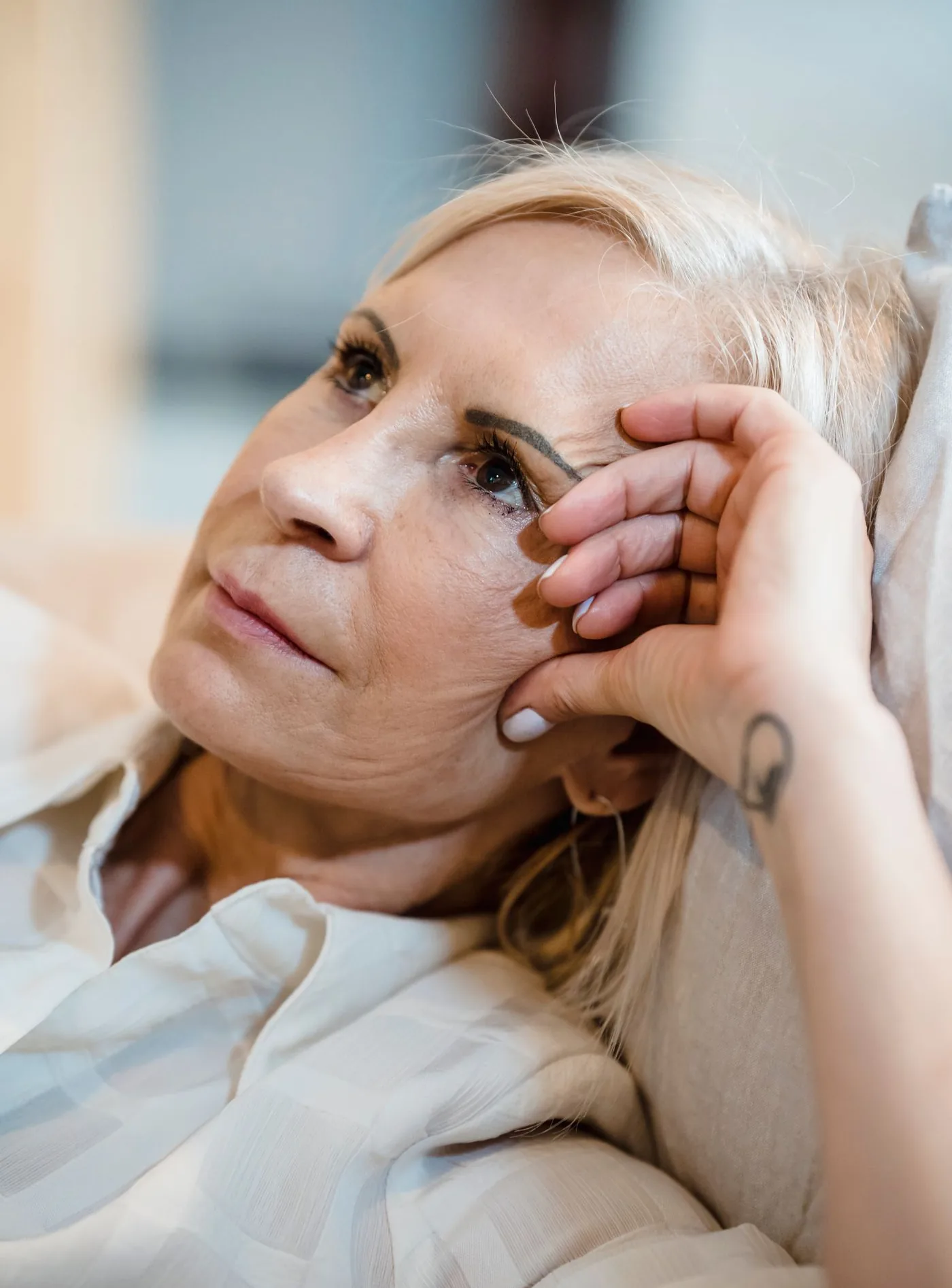Reife blonde Frau mit der Hand am Kopf und nachdenklichem Blick, Modellaufnahme zum Fadenlifting in Düsseldorf