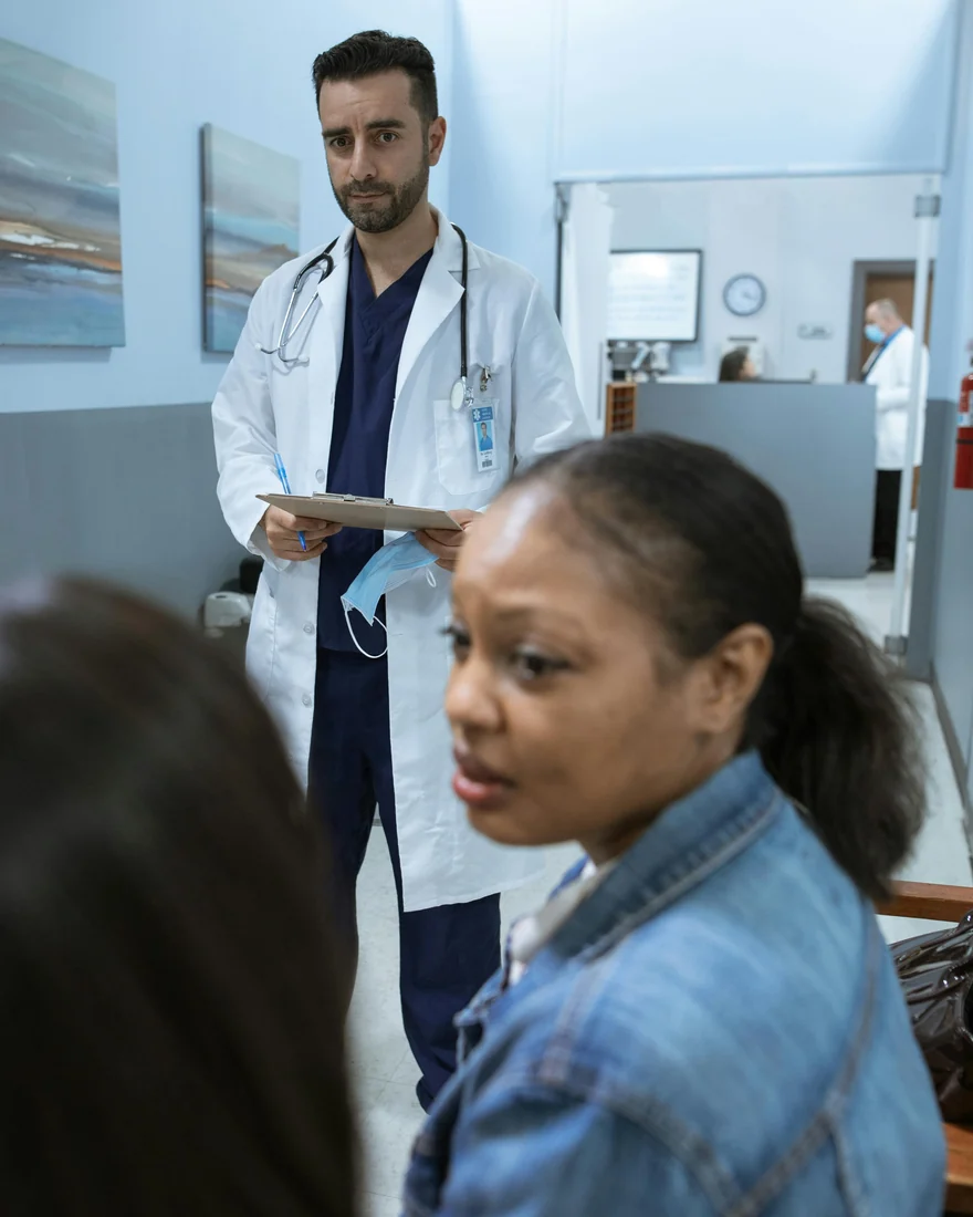 Arzt im weißen Kittel mit Klemmbrett im Gespräch mit einer Patientin in einem Klinikflur. Symbolbild für die Sprechstunde, in der die Fragen zum Brazilian Butt Lift gestellt werden