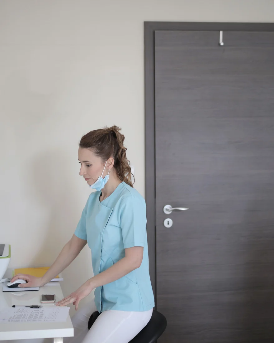 Medizinische Fachkraft an einem Anmeldetresen neben einer geschlossenen Behandlungszimmertür. Symbolbild für Eingriffe, die in der Praxis Fetai · Ästhetische Chirurgie nicht angeboten werden